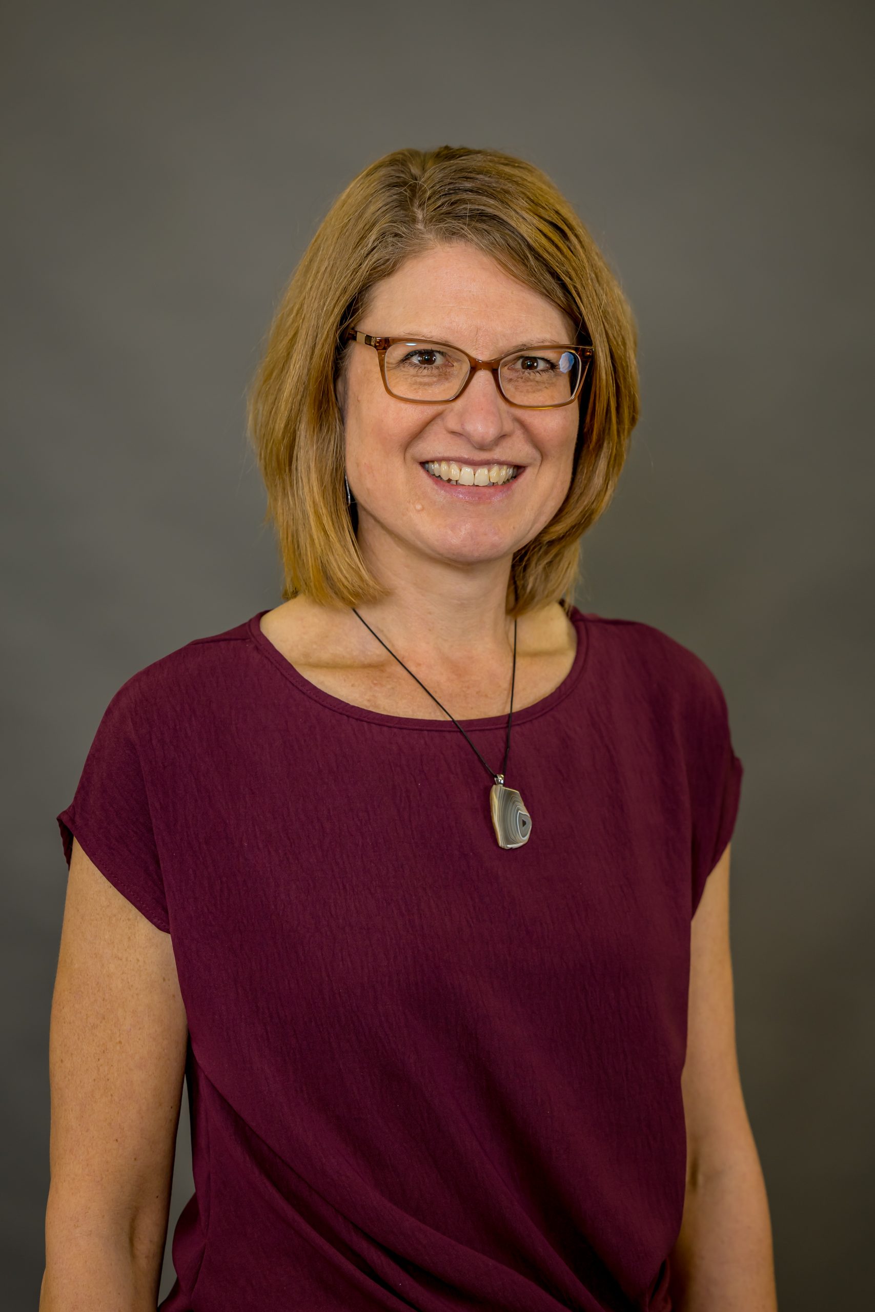 Mavis Melton, Physical Therapist at Spooner Health, smiling in a burgundy top with a pendant, professional portrait against a neutral background.