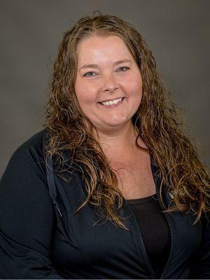 Erin VanGuilder, Certified Occupational Therapy Assistant (COTA) at Spooner Health, smiling with curly hair, wearing a black top, emphasizing her role in outpatient therapy and rehabilitation services.